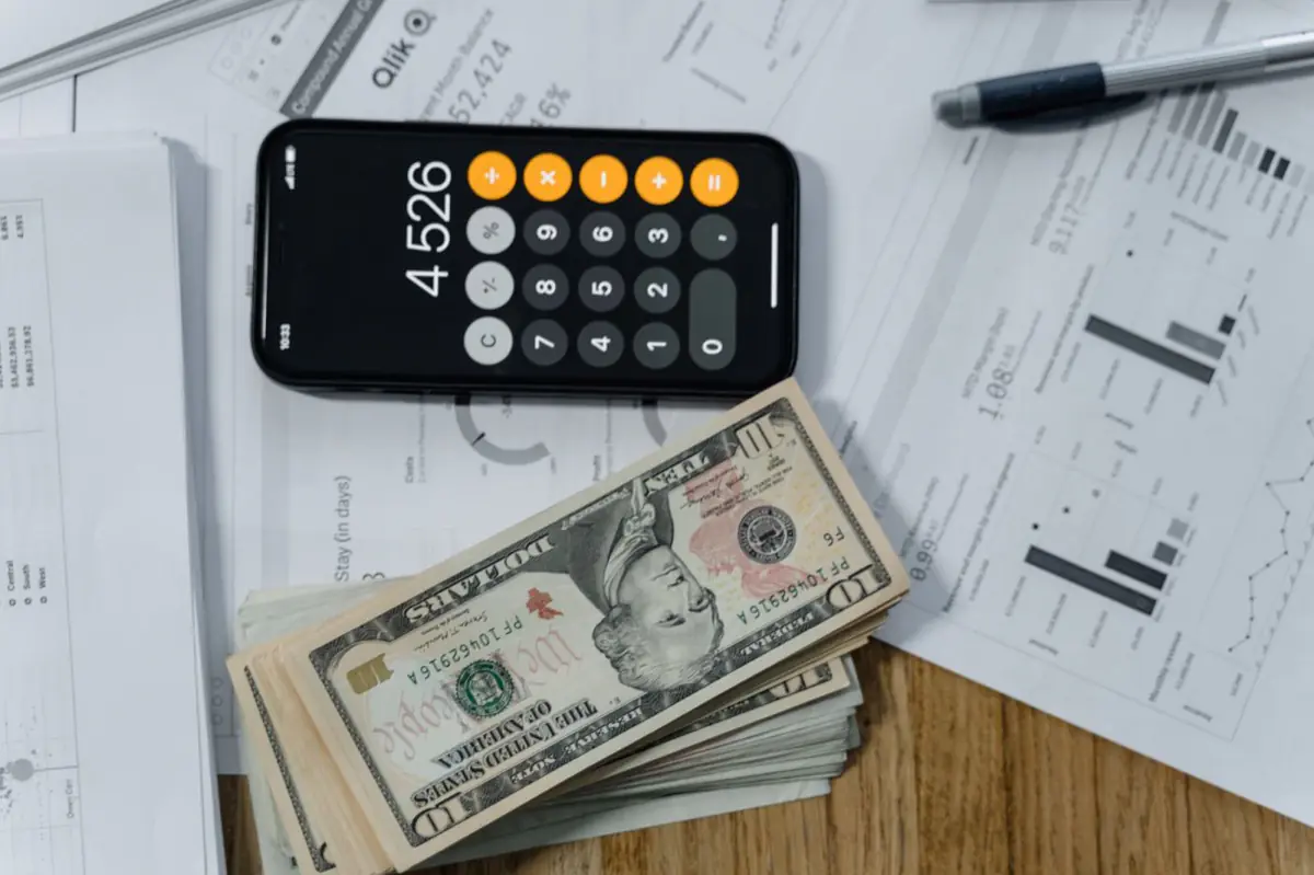 A phone calculator, cash and printed financial reports on a desk