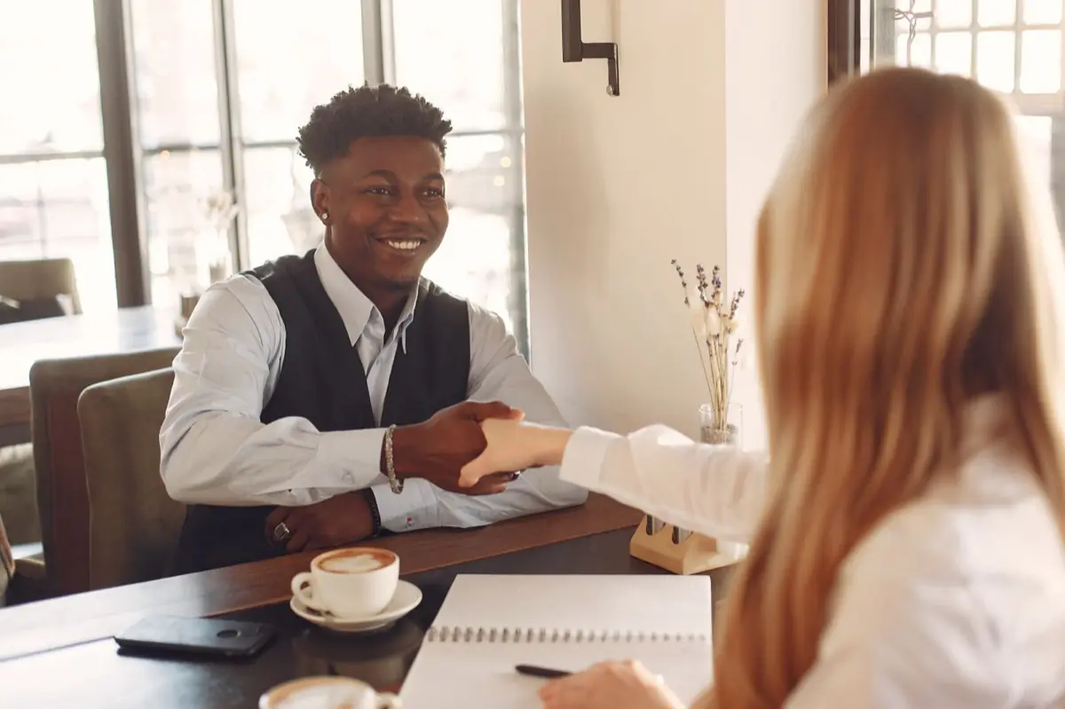 Two people shaking hands across a table in a cafe