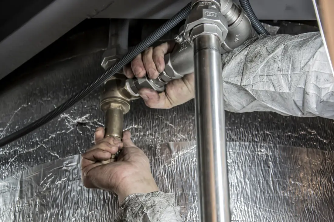 A plumber fitting pipework under a sink